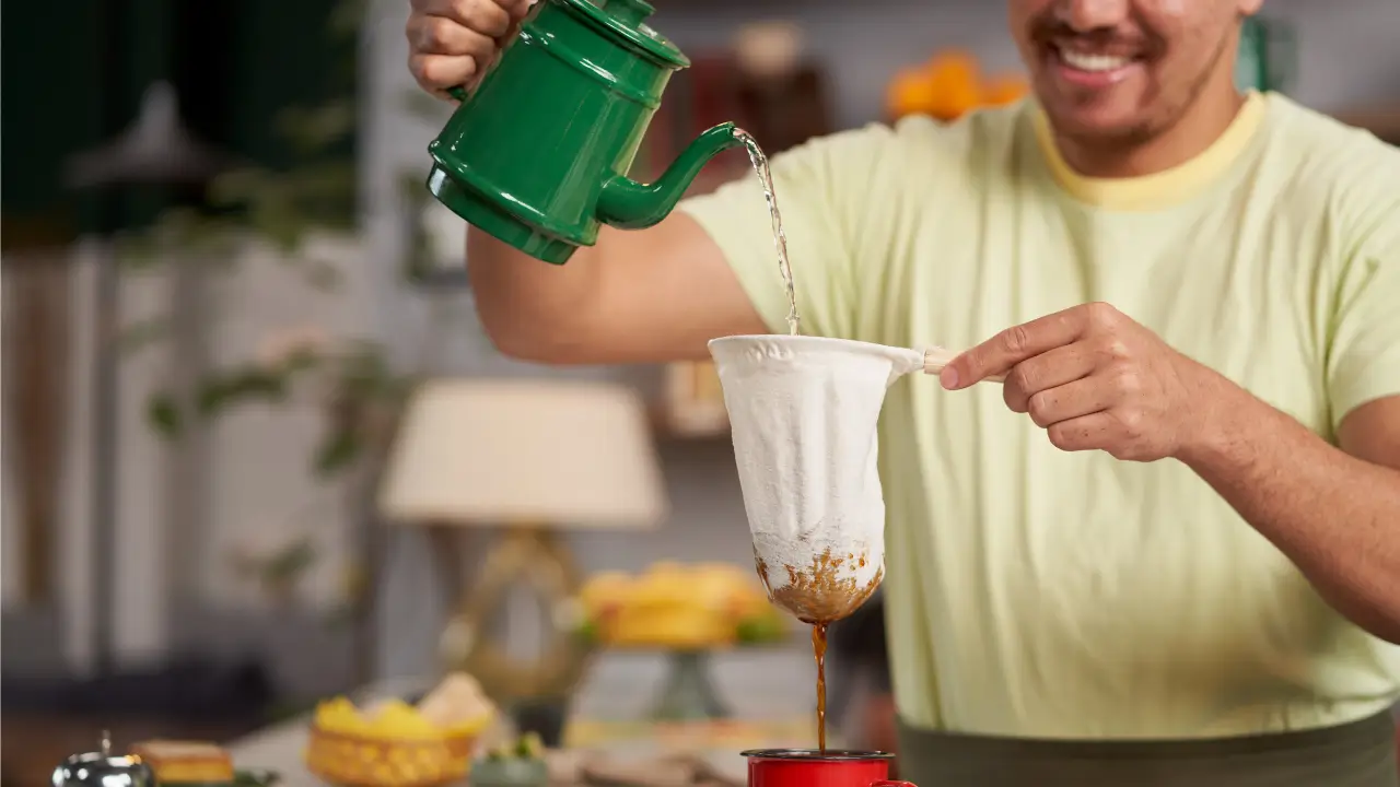 homem passando um café especial com sorriso no rosto em uma cozinha bem brasileira